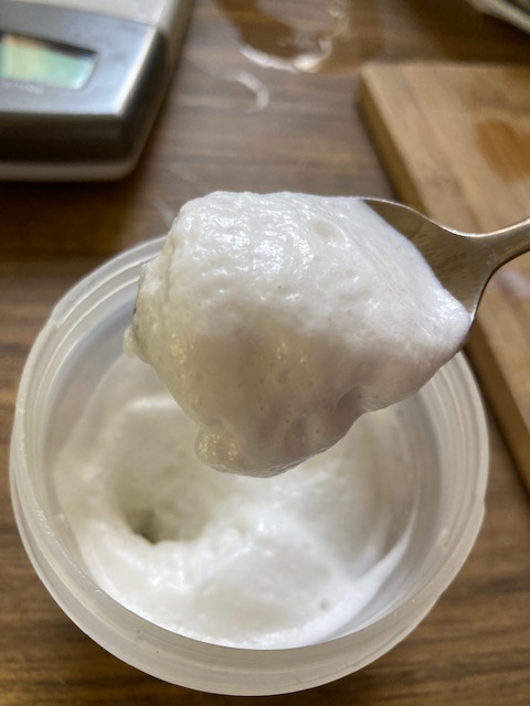 A spoon is held over a bowl. Both the spoon and bowl hold a thick white mixture