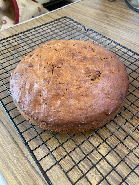 A flat brown cake sits on a wire cooling rack
