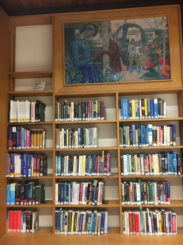 A painting and some books on shelves at Wheatley Library.
Wooden book shelves filled with books. Above the books is the painting 'Omega' by Evelyn Dunbar.
