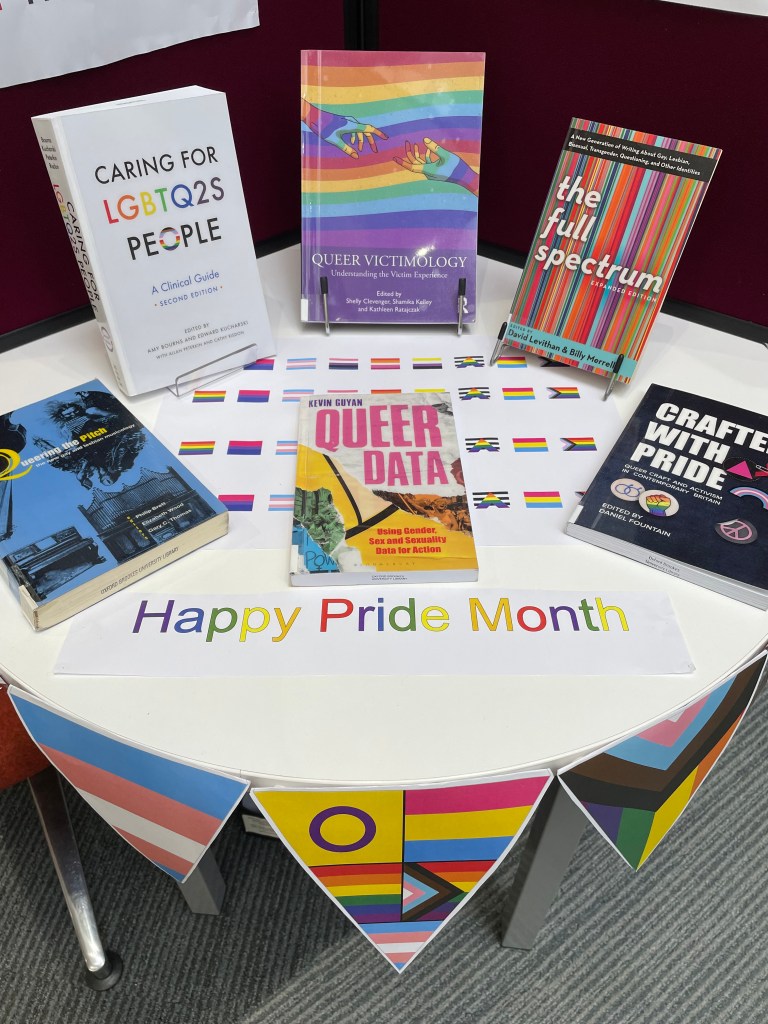 A table is bordered with rainbow flag bunting and topped with six books on LGBTQ+ themes